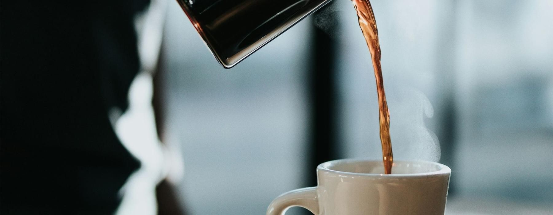 a person pouring a carafe of coffee into a cup